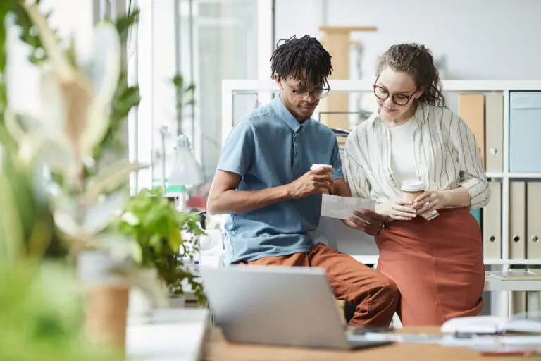 Portrait of two creative young people looking at printed photographs during coffee break in modern office, copy space